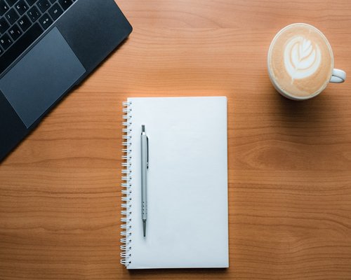 A notebook, pen, and coffee cup on a tidy desk